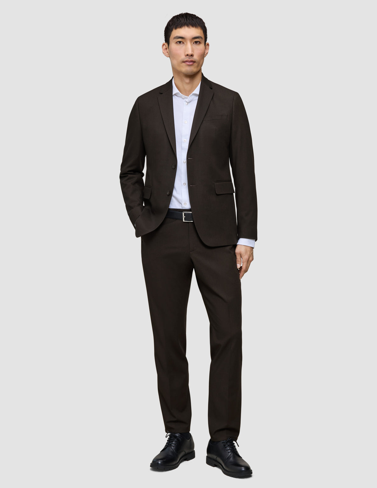En mann kledd i en Motion Blazer Slim Cognac, hvit skjorte, svart belte og svarte dressko.