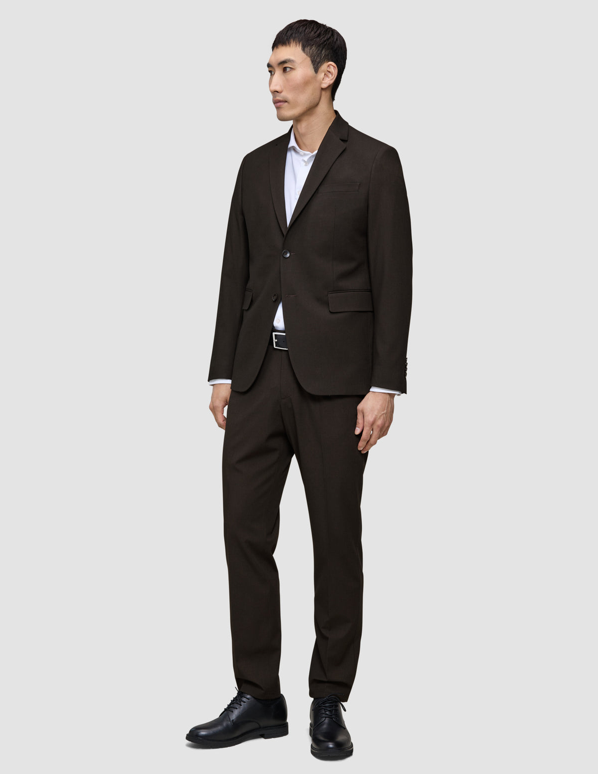 En mann i en Motion Blazer Slim i fargen Cognac og mørkebrune bukser, med hvit skjorte og svarte dressko.