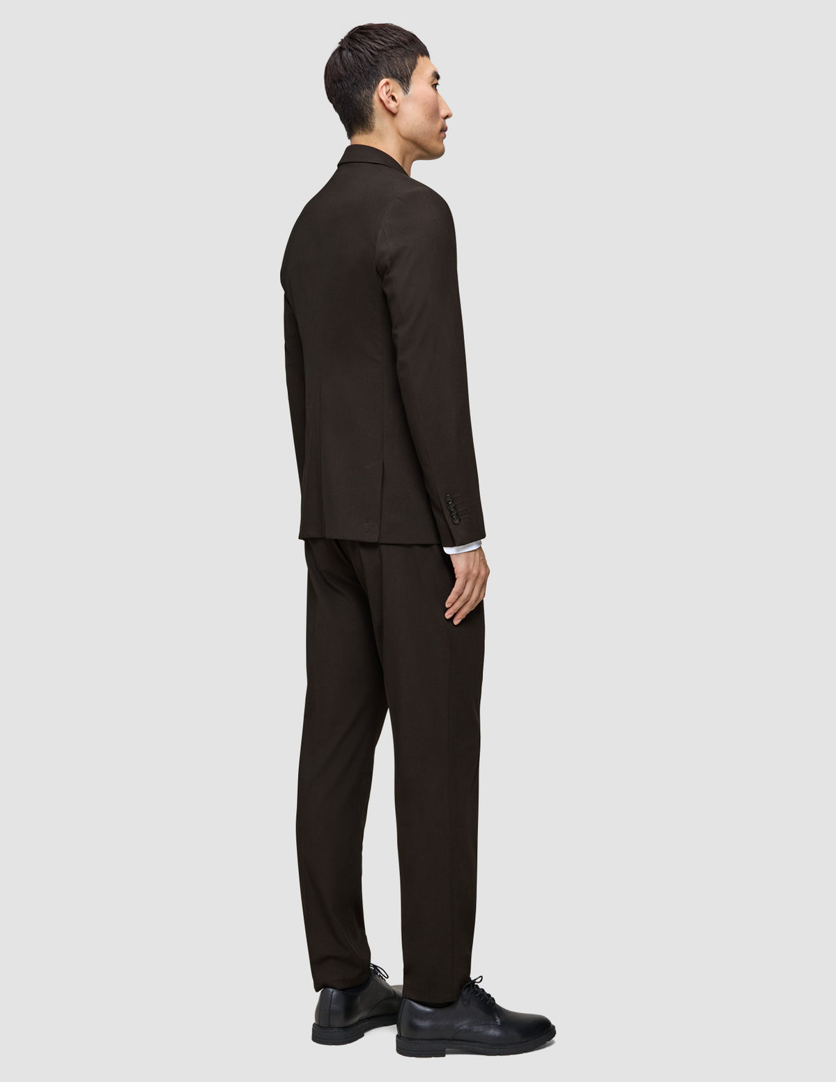 En mann sett bakfra, kledd i en Motion Blazer Slim Cognac og mørkebrune slim-fit-bukser med svarte skinnsko.