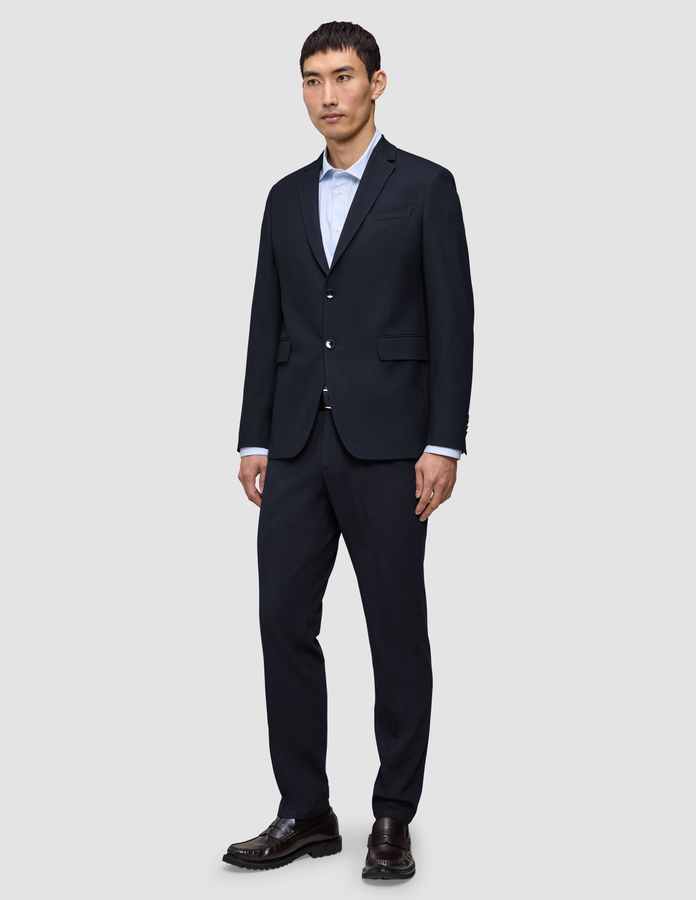 En mann i en Motion Blazer Slim-jakke i midnattsblått, matchende bukser, en lyseblå skjorte og brune loafers.