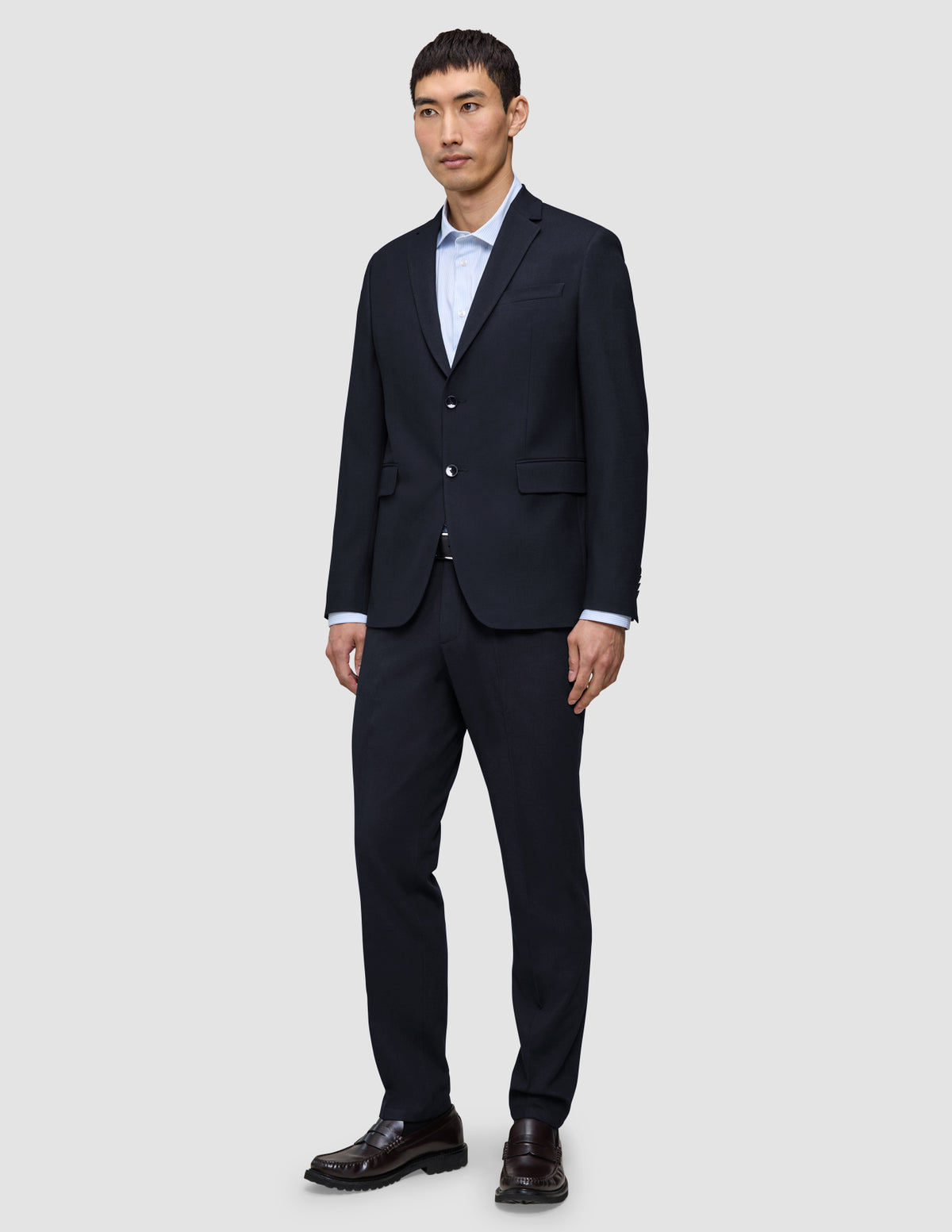En mann i en Motion Blazer Slim-jakke i midnattsblått, matchende bukser, en lyseblå skjorte og brune loafers.