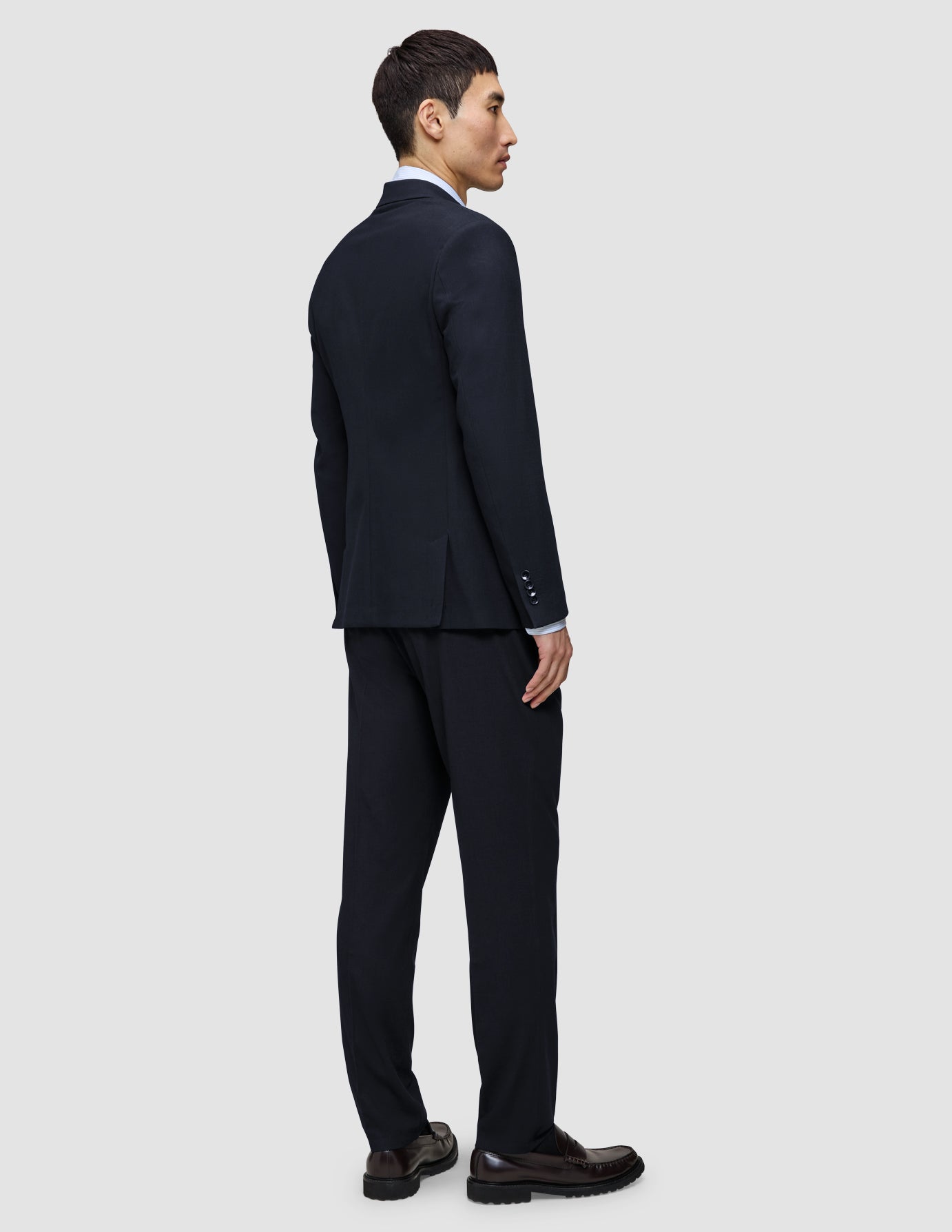 En mann sett bakfra, kledd i en Motion Blazer Slim i fargen Midnight Blue, med matchende bukser og loafers.