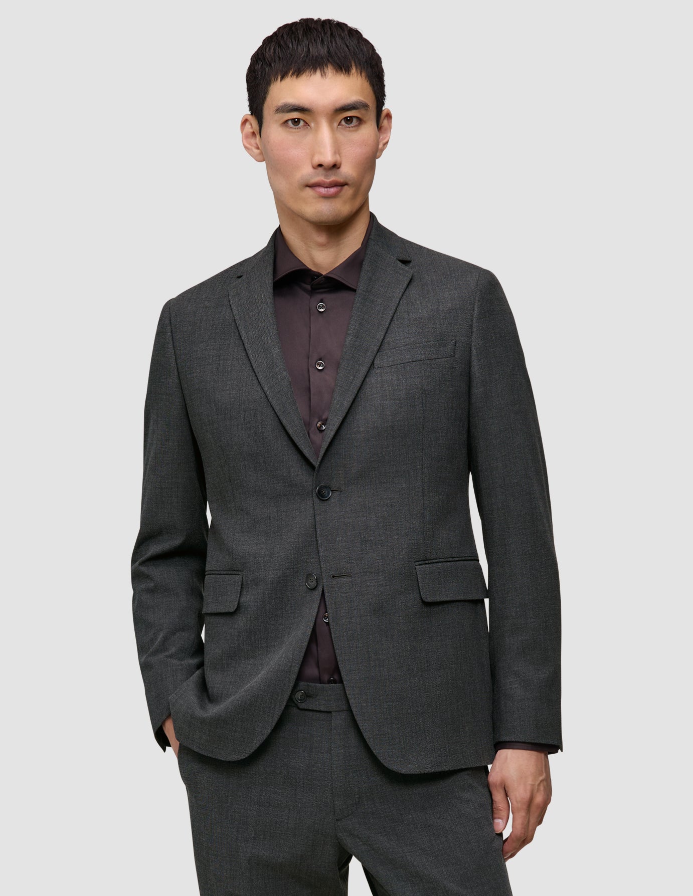 En mann som har på seg en grå Motion Blazer Slim Pepper Grey over en mørk skjorte med knapper.