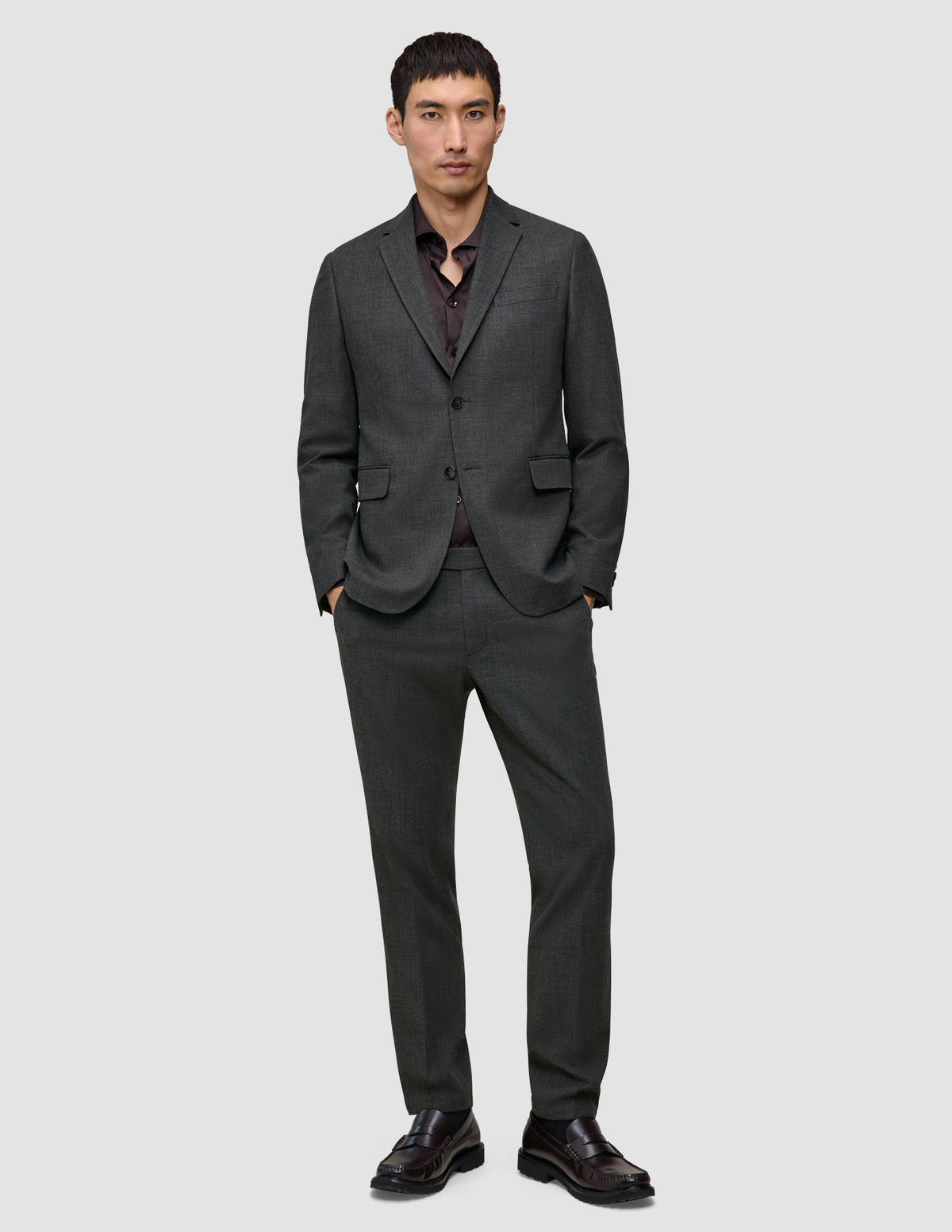 En mann kledd i en Motion Blazer Slim Pepper Grey-jakke, matchende bukser, mørk skjorte og loafers.