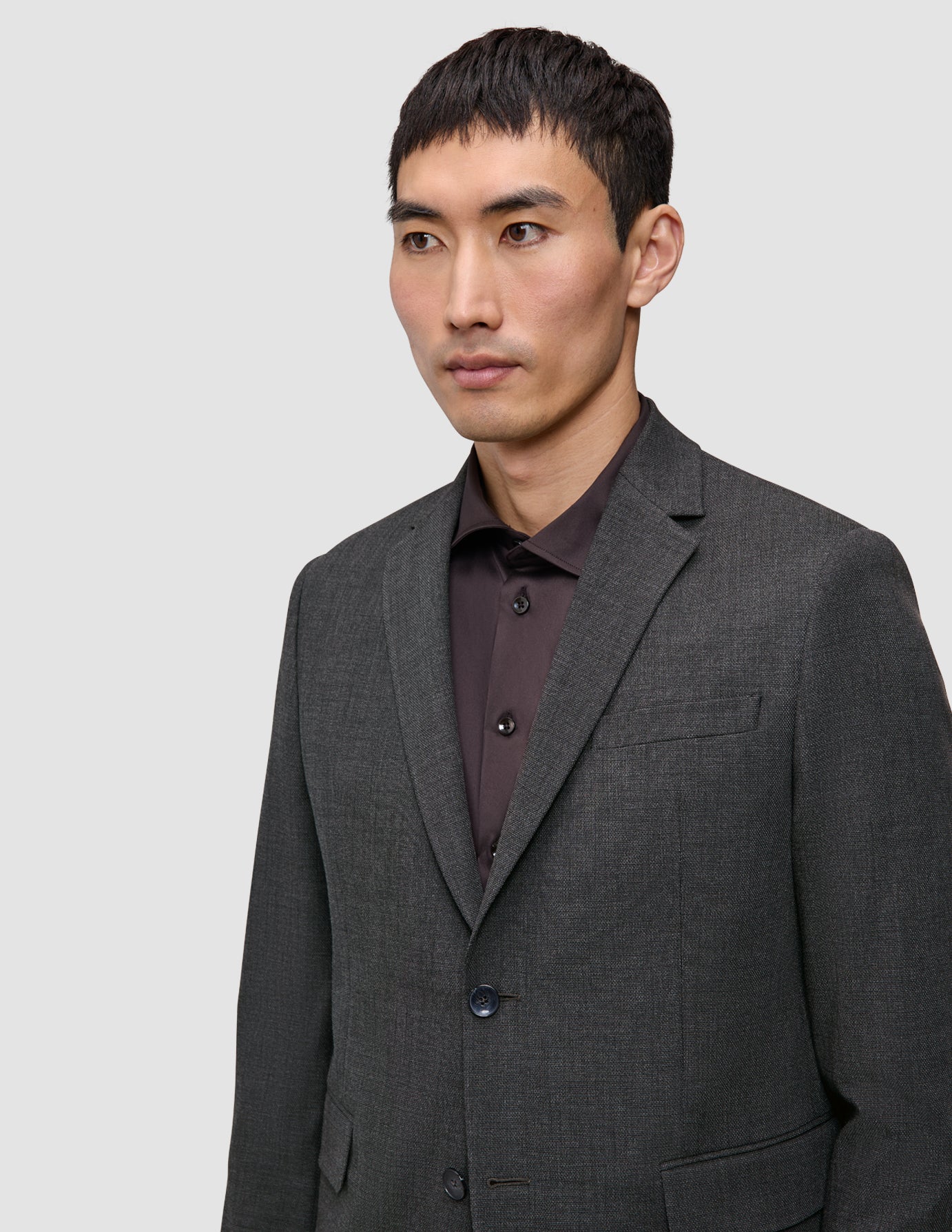 En mann som har på seg en skreddersydd Motion Blazer Slim Pepper Grey-blazer over en mørk skjorte med knapper.