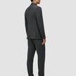 En mann sett bakfra, kledd i en grå Motion Blazer Slim i fargen Pepper Grey og mørke loafers, som fremhever det elegante skandinaviske designet.