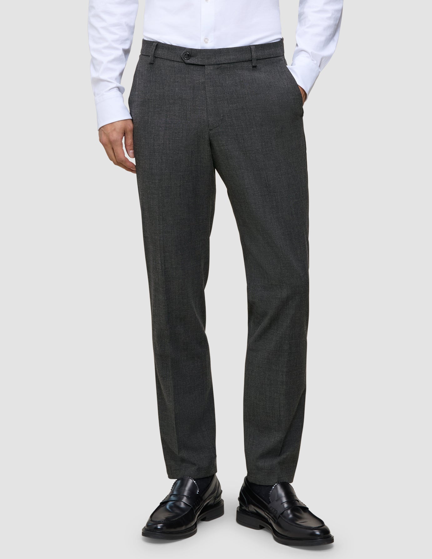 En mann i en hvit skjorte med knapper, svarte skinnloafers og Motion Suit-bukser i Regular-passform i fargen Pepper Grey.