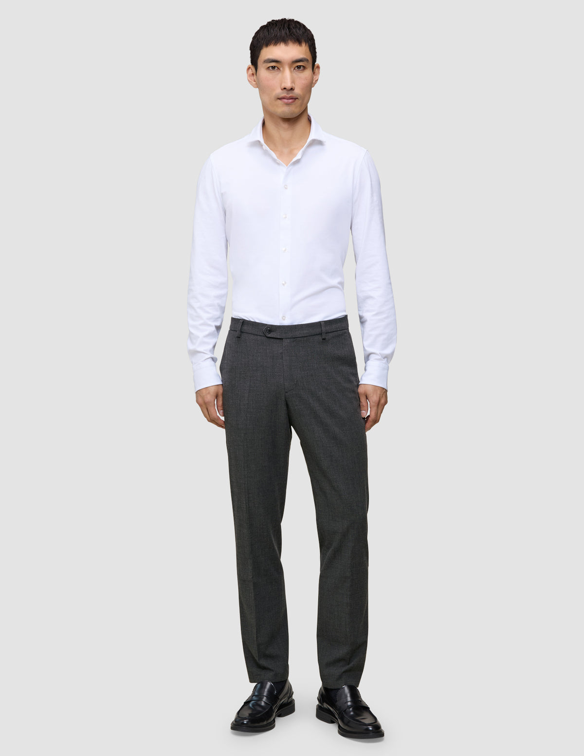 En mann i en hvit skjorte med knapper og Motion Suit-bukser i Regular-passform i fargen Pepper Grey med 360°-stretch.