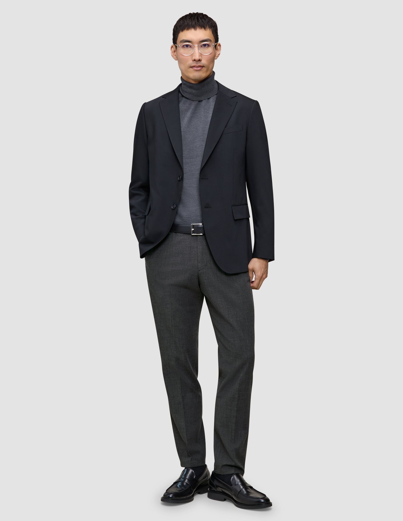 En mann i svart blazer, grå turtleneck, Motion Suit-bukser i Regular-passform i fargen Pepper Grey og svarte loafers.