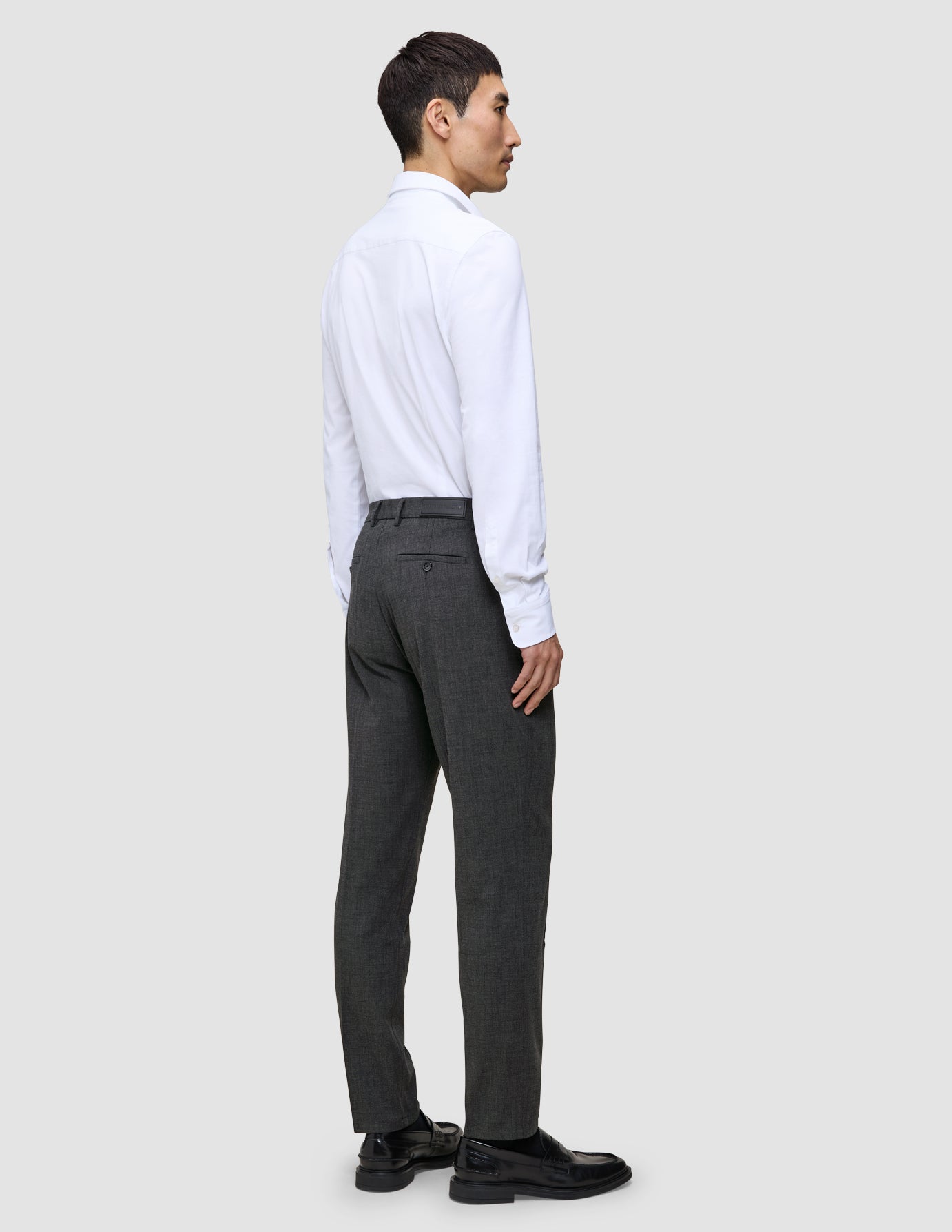 En mann i hvit skjorte og grå Motion Suit-bukse i Regular-passform i fargen Pepper Grey, sett bakfra.