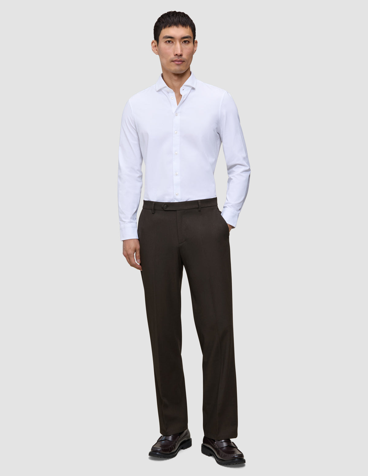 En mann i en hvit skjorte med knapper og Motion Suit-bukser i modellen Relaxed Cognac, med et rent skandinavisk design.