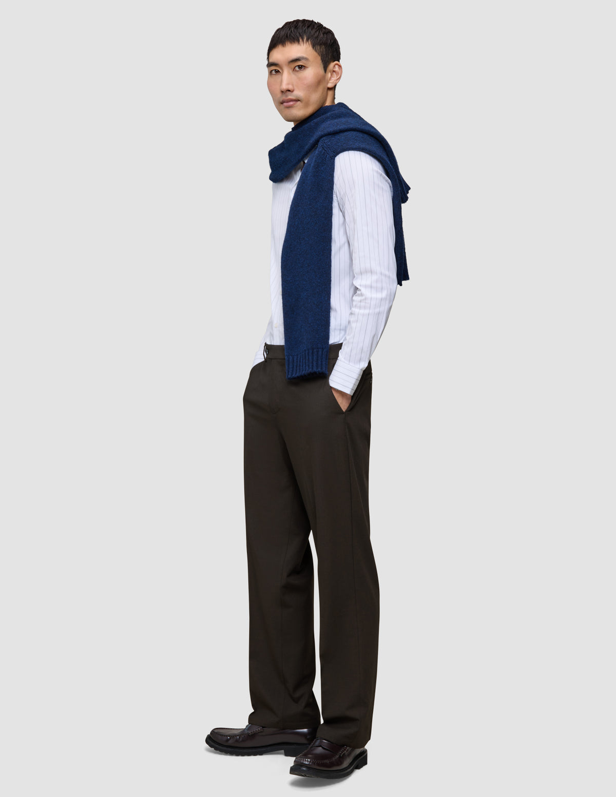 En mann i en hvit skjorte med smale striper, en marineblå genser og Motion Suit Pants Relaxed Cognac med 360°-stretch.