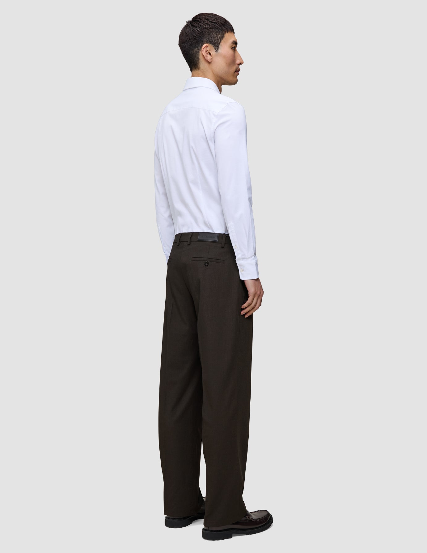 En person sett i profil har på seg en hvit skjorte med knapper og Motion Suit-bukser i modellen Relaxed i fargen Cognac.