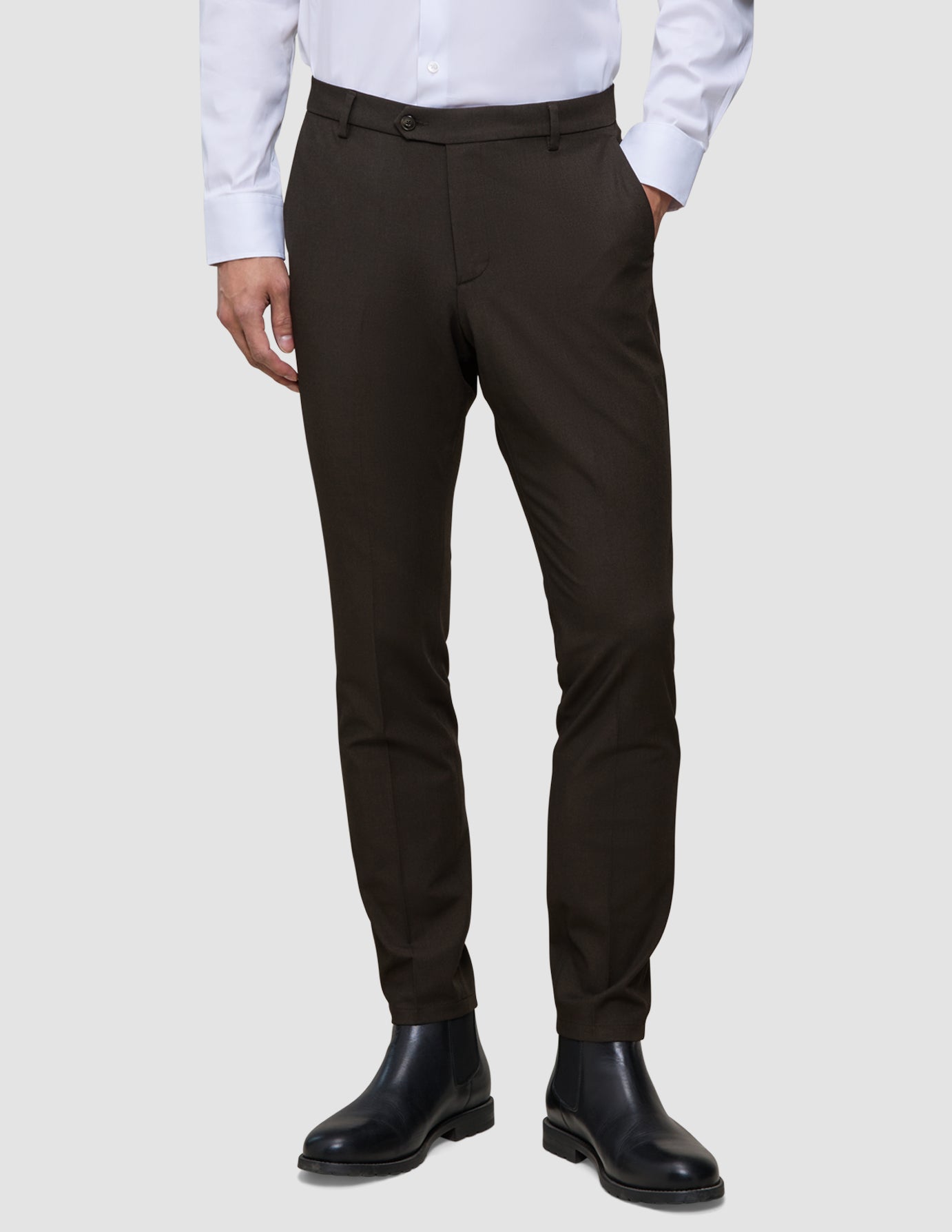 Mørkebrune Motion-dressbukser i slim fit-modell, Slim Cognac, kombinert med en hvit skjorte med knapper og svarte lærstøvler.