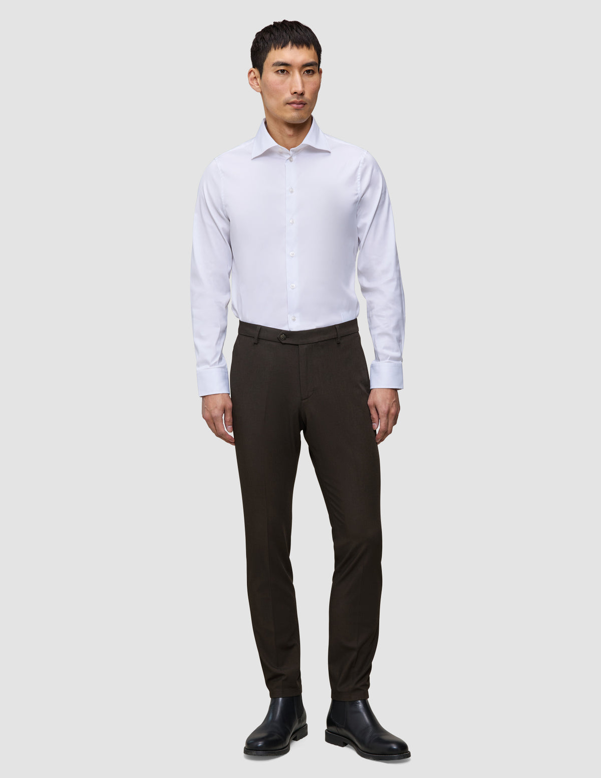 En mann i hvit skjorte, Motion Suit-bukser i slim-passform i fargen Cognac og svarte lærstøvler med 360°-stretch.
