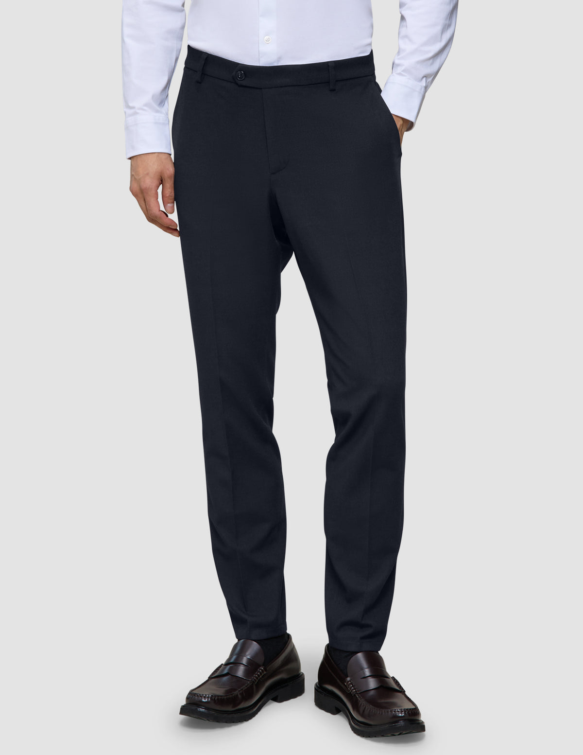 Motion Suit Pants Slim – Midnattsblå dressbukser i slim fit, kombinert med en hvit skjorte med knapper og brune loafers.