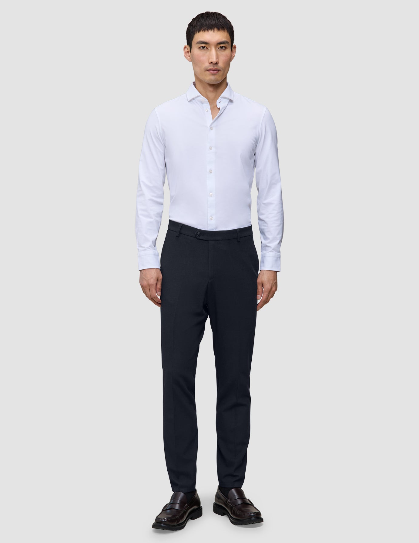 En mann i en hvit skjorte med knapper, midnattsblå Motion Suit Pants Slim og brune loafers.