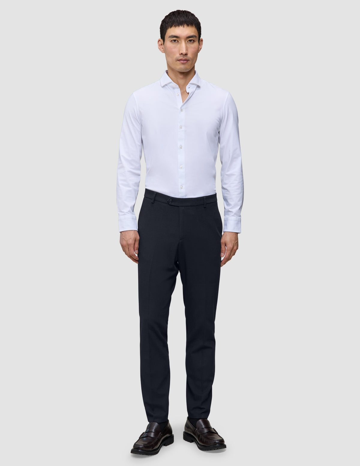 En mann i en hvit skjorte med knapper, midnattsblå Motion Suit Pants Slim og brune loafers.