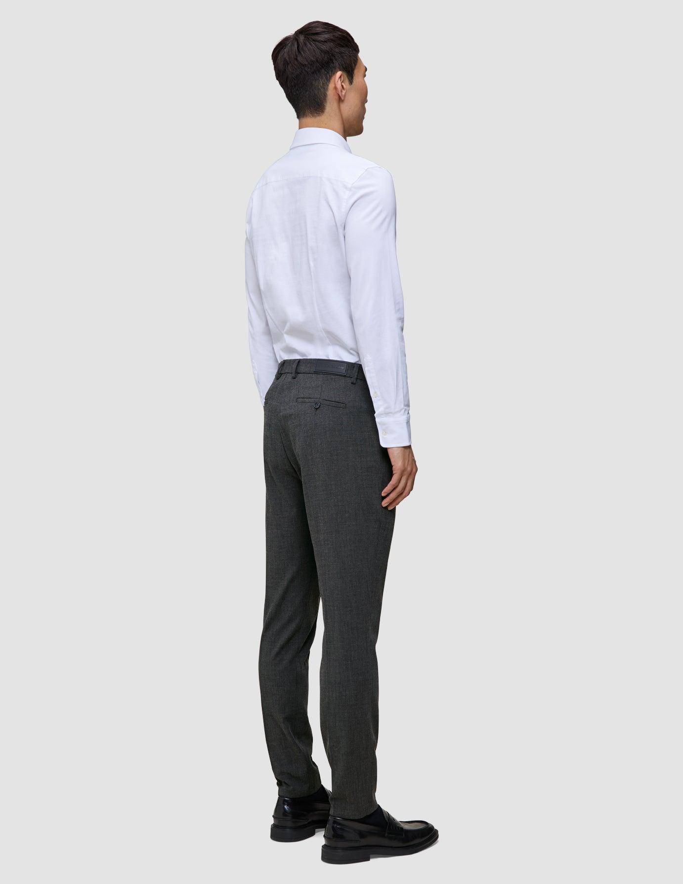 En mann i en hvit skjorte med knapper og Motion Suit-bukser i fargen Slim Pepper Grey, sett bakfra.