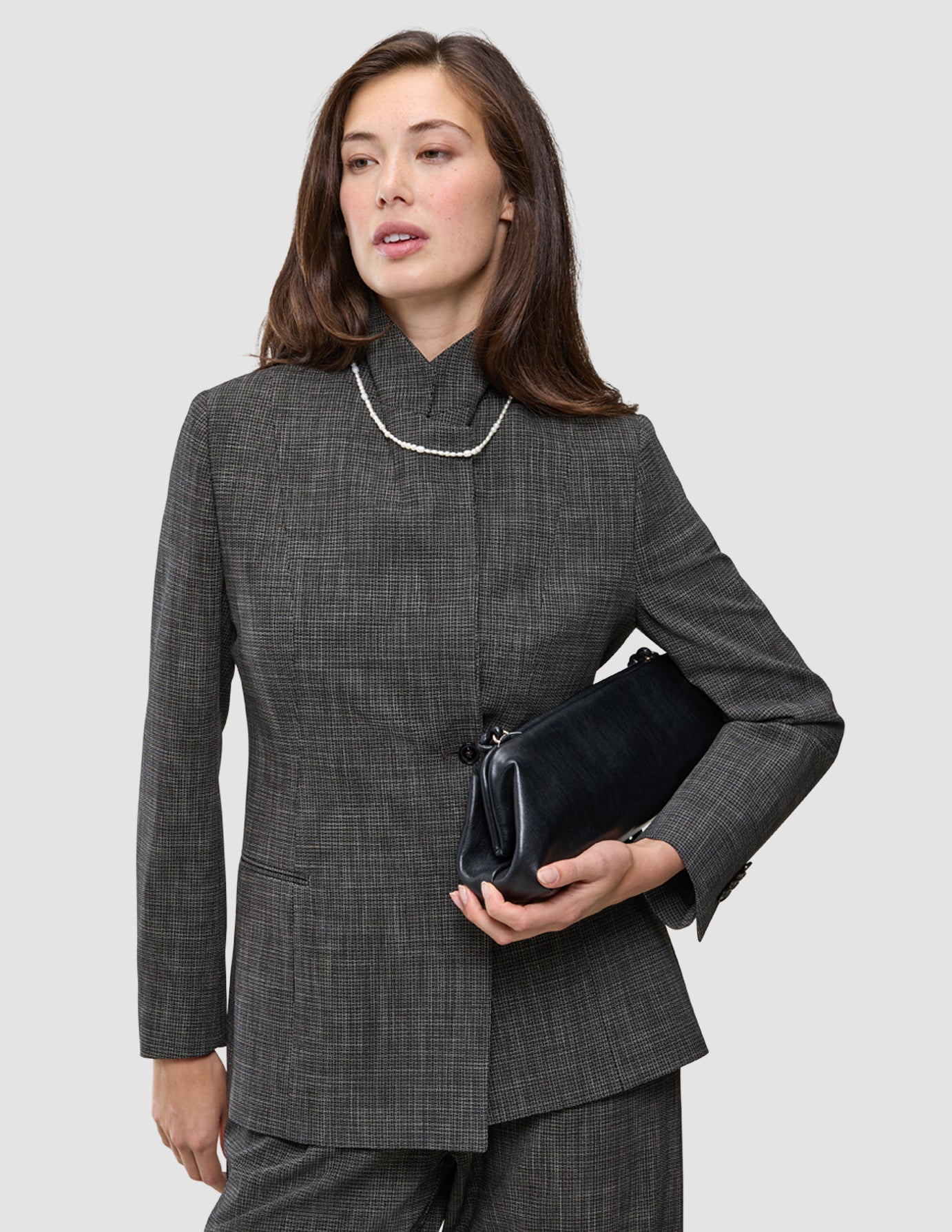 En kvinne i et dress med karakter, med klassiske ruter, et perlekjede og en svart clutch.