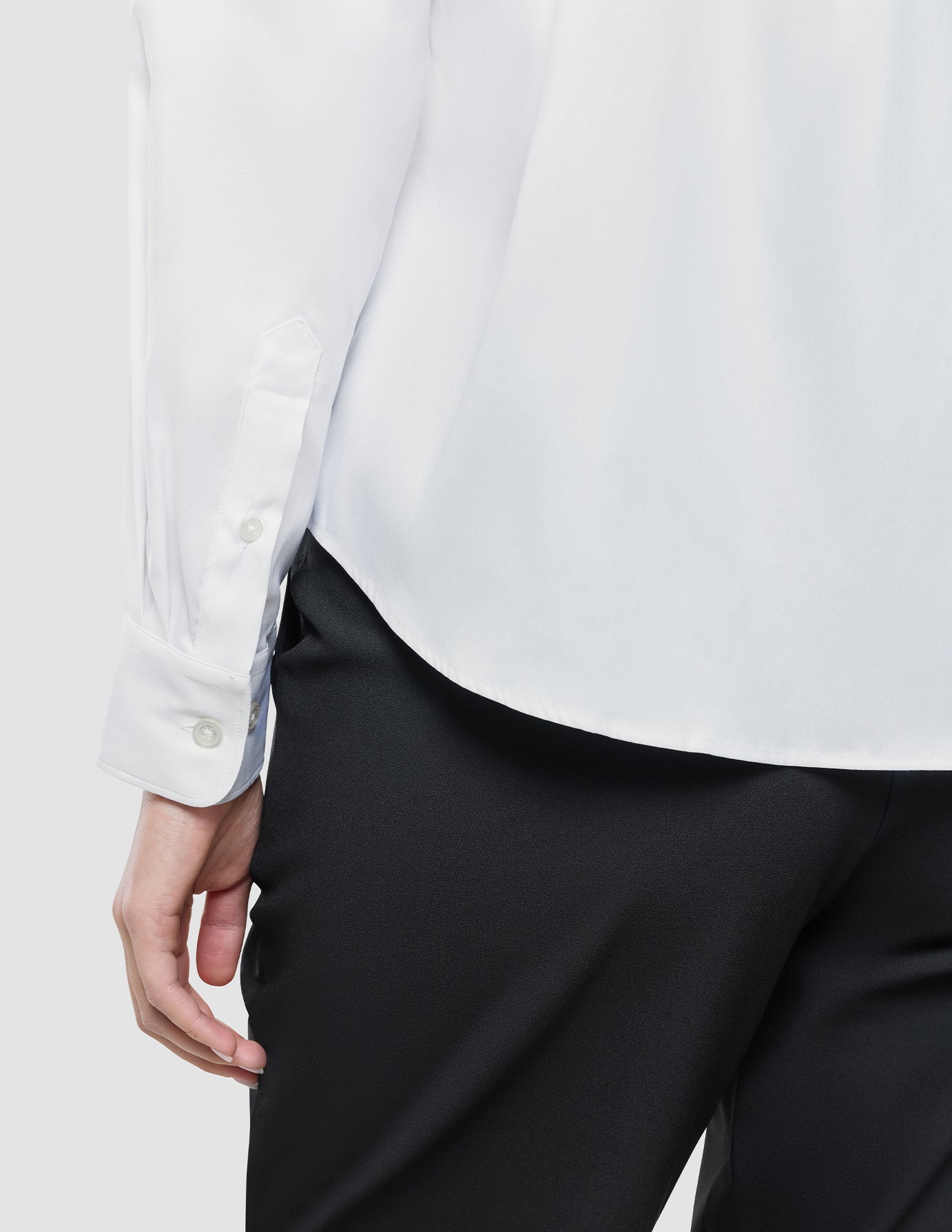 En person kledd i en hvit «Women Oxford Shirt» i vanlig passform og svarte bukser, som gjenspeiler en sofistikert skandinavisk estetikk.