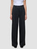 En person som har på seg de svarte Serene Pants Wide Black-buksene med plissering foran og en hvit T-skjorte i skandinavisk stil.