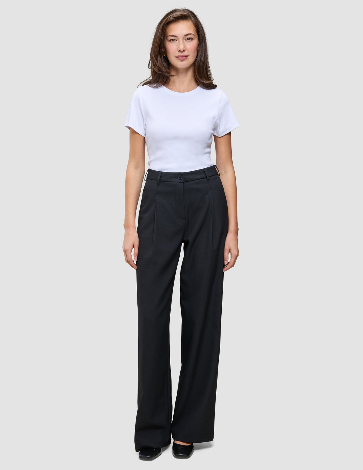 En kvinne iført en hvit T-skjorte og svarte Serene Pants Wide Black-bukser med høy midje og vide ben.