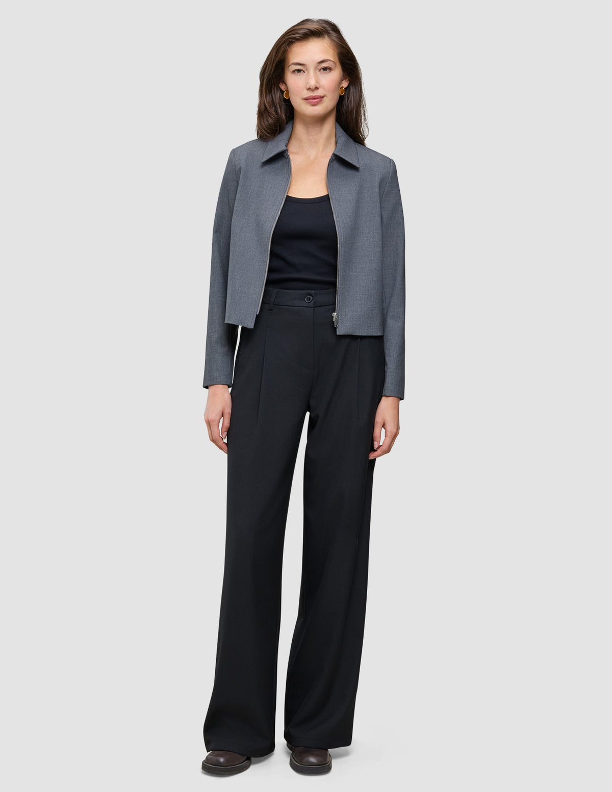 En kvinne har på seg en grå, kort jakke, en svart tank-top og svarte Serene Pants Wide Black.