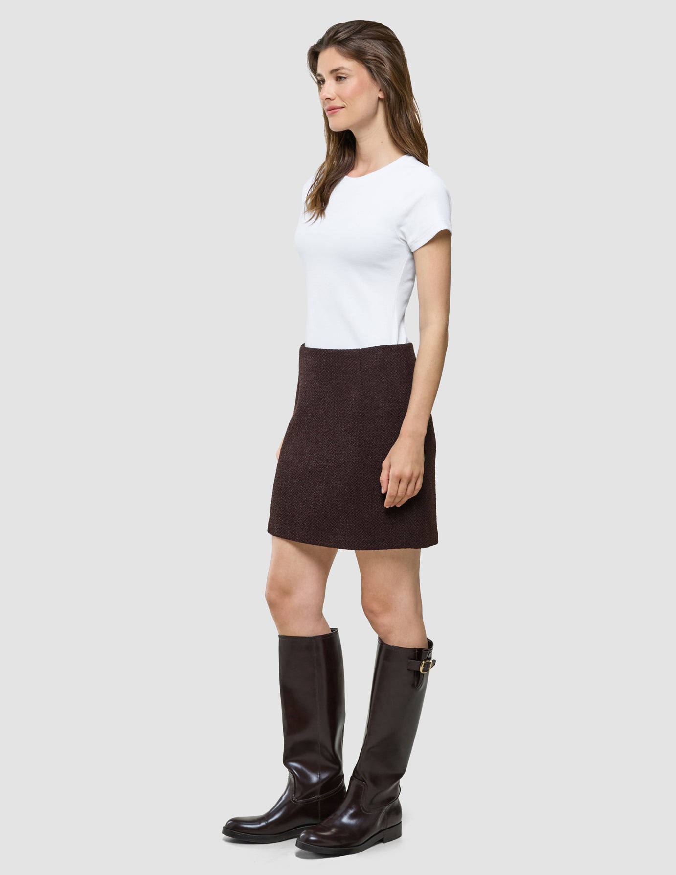 En kvinne i en hvit T-skjorte, «Women Sorae Short Skirt Espresso» og høye brune støvler.