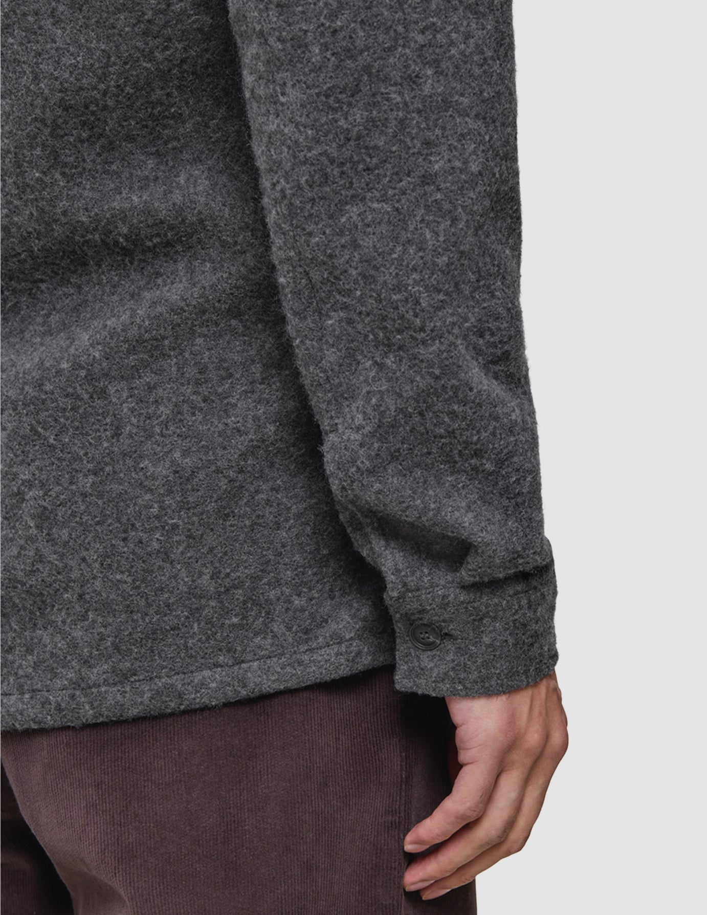 En person har på seg en uformell, diskret antracittgrå ullskjorte med knappede mansjetter og mørkebrune jeans.
