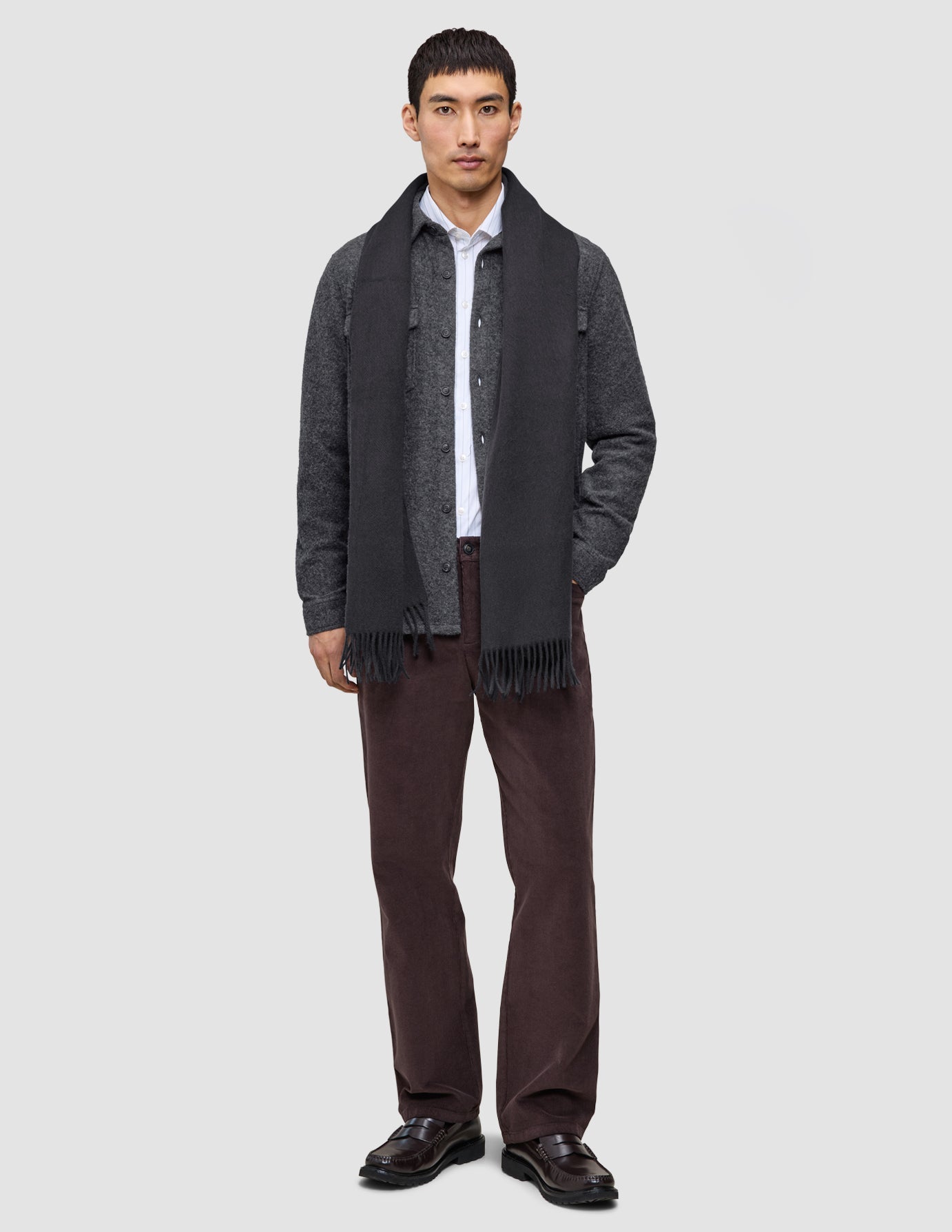 En mann har på seg et langt skjerf over en skjorte med knapper, et grått Casual-plagg med gjennomtenkt design og mørke Marco-jeans.