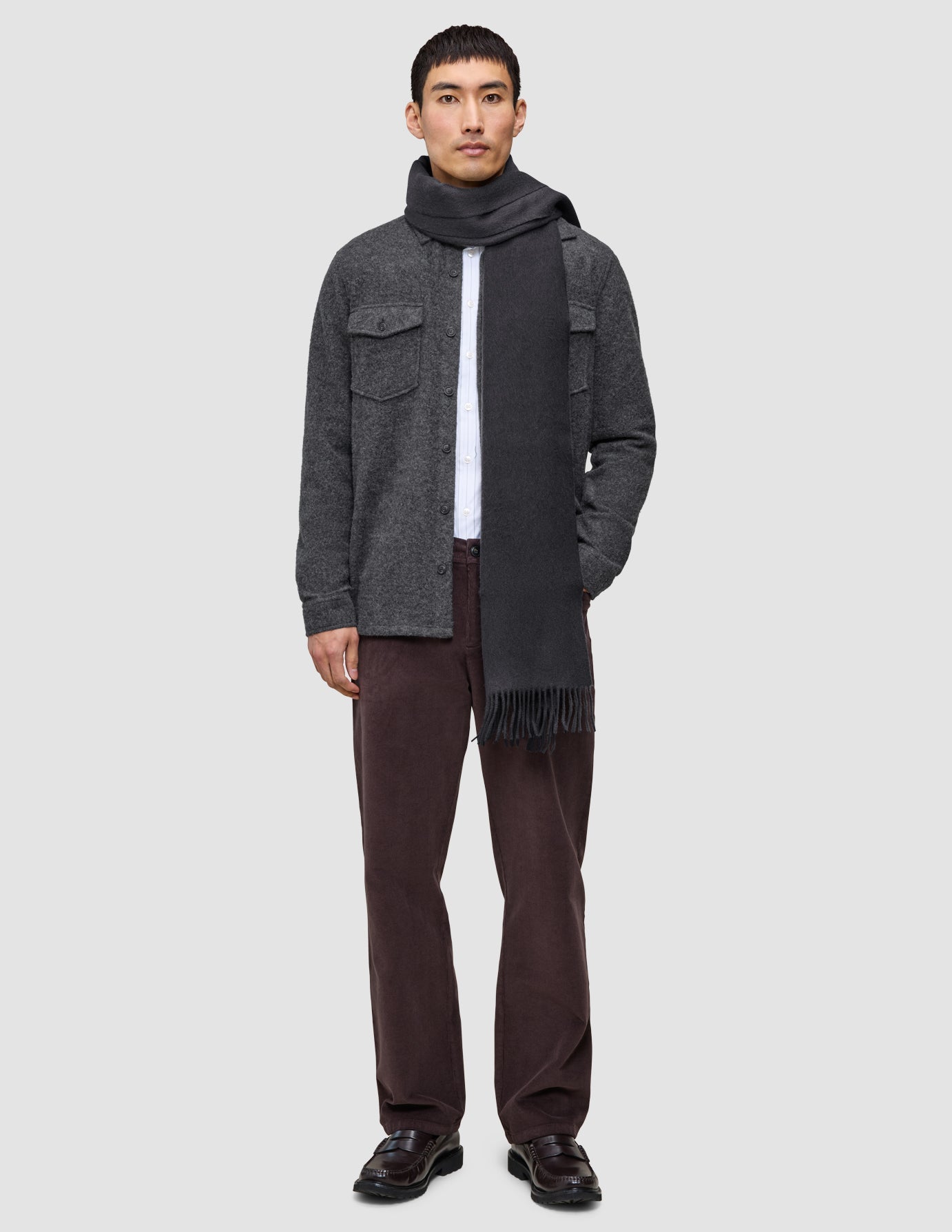 En mann kledd i en uformell og gjennomtenkt to-lags ullskjorte, hvit skjorte, brune Marco-jeans og et langt grått skjerf.
