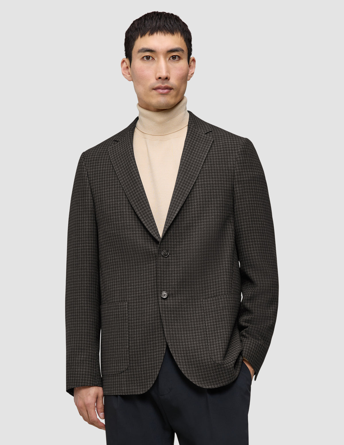 En mann som har på seg en Timeless Wool Blazer Slim i mørkebrun rutemønster over en beige turtleneck-genser.
