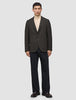 En mann har på seg en Timeless Wool Blazer Slim i mørkebrun rutemønster over en beige turtleneck og mørke bukser.
