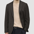 En person har på seg en Timeless Wool Blazer Slim i mørkebrun rutemønster over en beige turtleneck og svarte bukser.