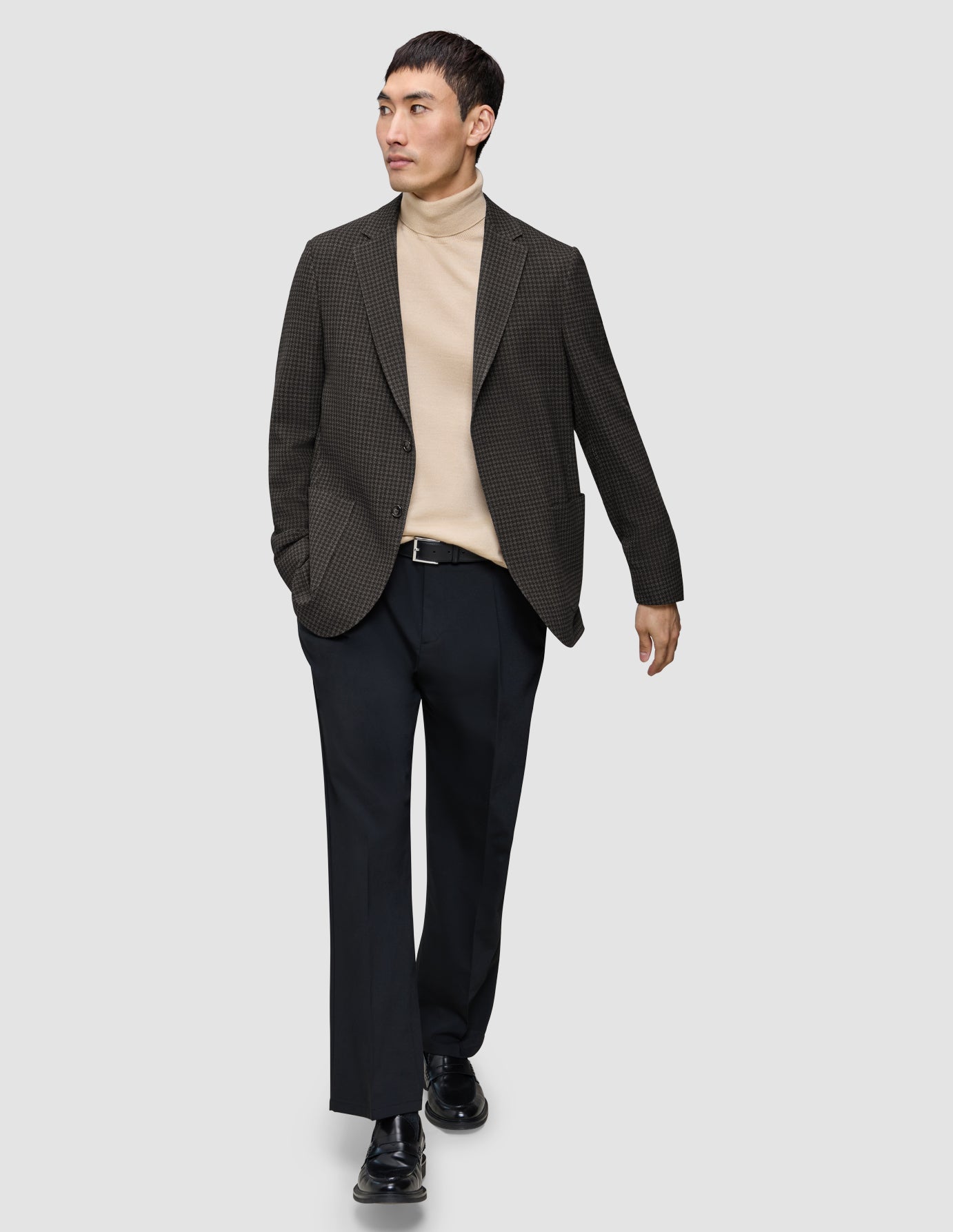 En mann kledd i en Timeless Wool Blazer Slim i mørkebrun rutemønster, beige turtleneck, svarte bukser og loafers.