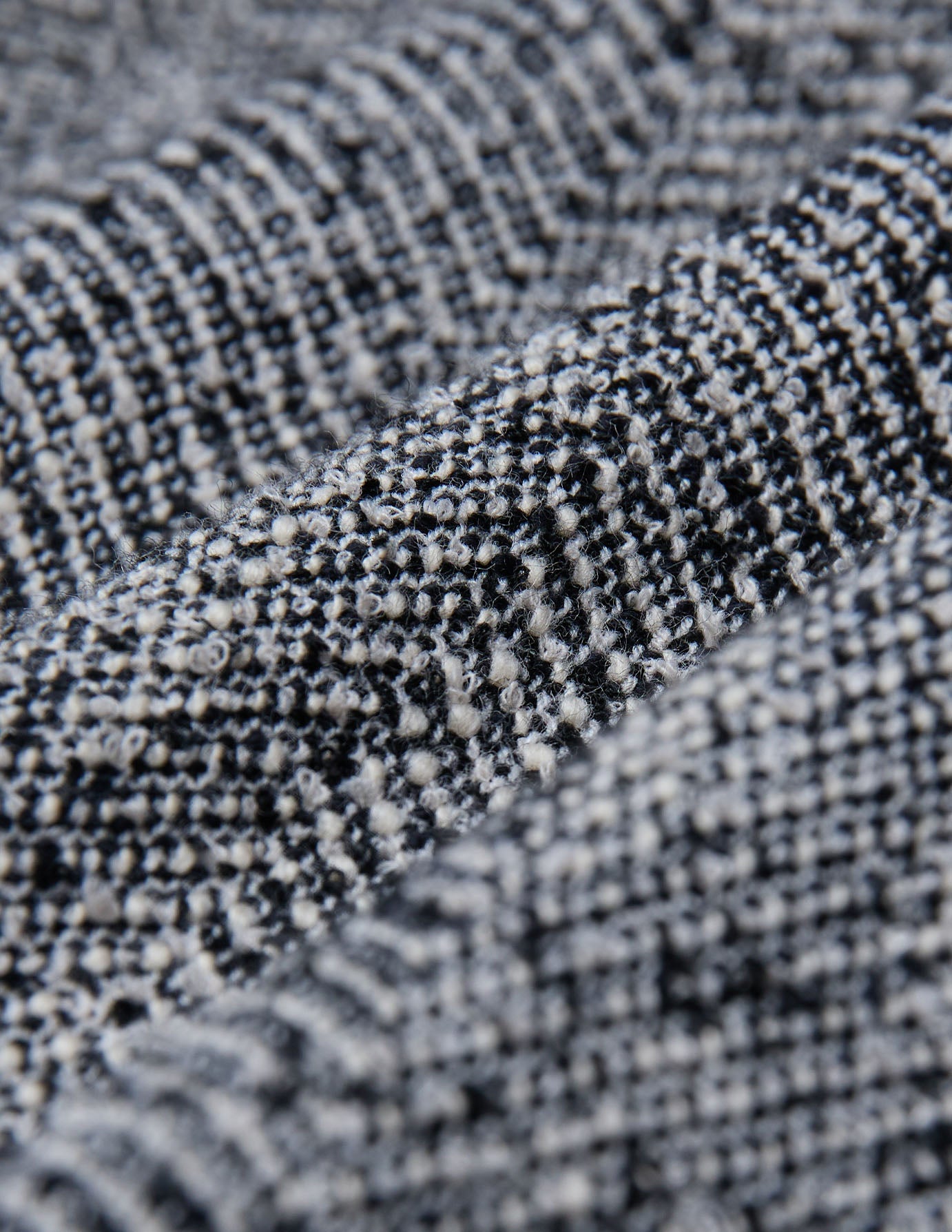 Nærbilde av det svart-hvite, strukturerte bouclé-stoffet med fiskebeinmønster som er brukt til damebuksene Ashryn Pants Wide Domino Herringbone.