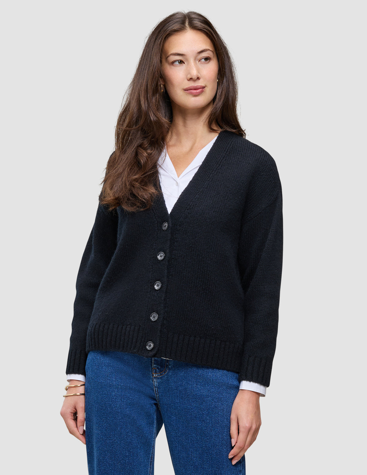 En kvinne som har på seg en svart, grovstrikket, myk ullcardigan for kvinner over en hvit skjorte med krage og blå jeans.