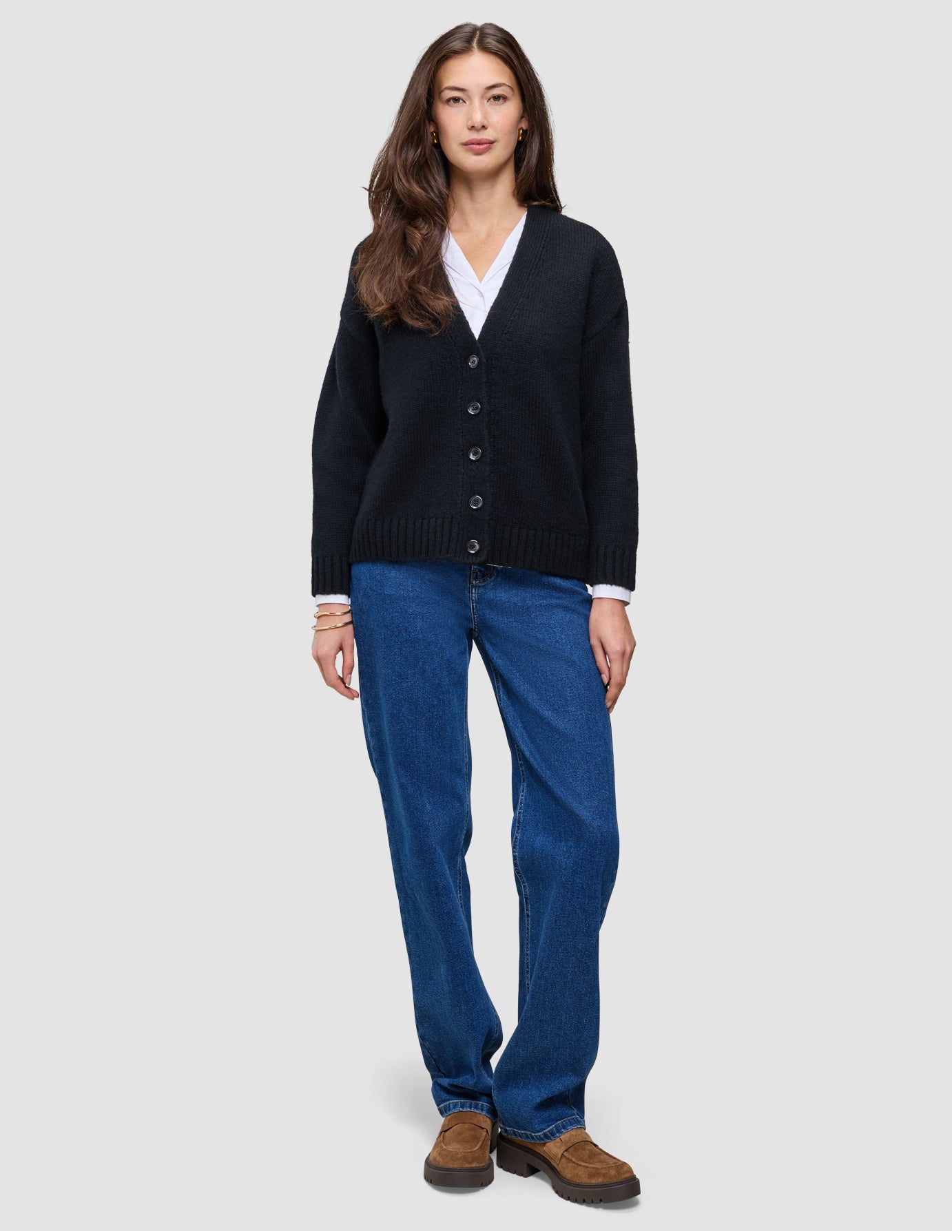 En person som har på seg en svart, grovstrikket, myk ullcardigan for kvinner over en hvit skjorte og blå jeans.