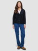 En person som har på seg en svart, grovstrikket, myk ullcardigan for kvinner over en hvit skjorte og blå jeans.