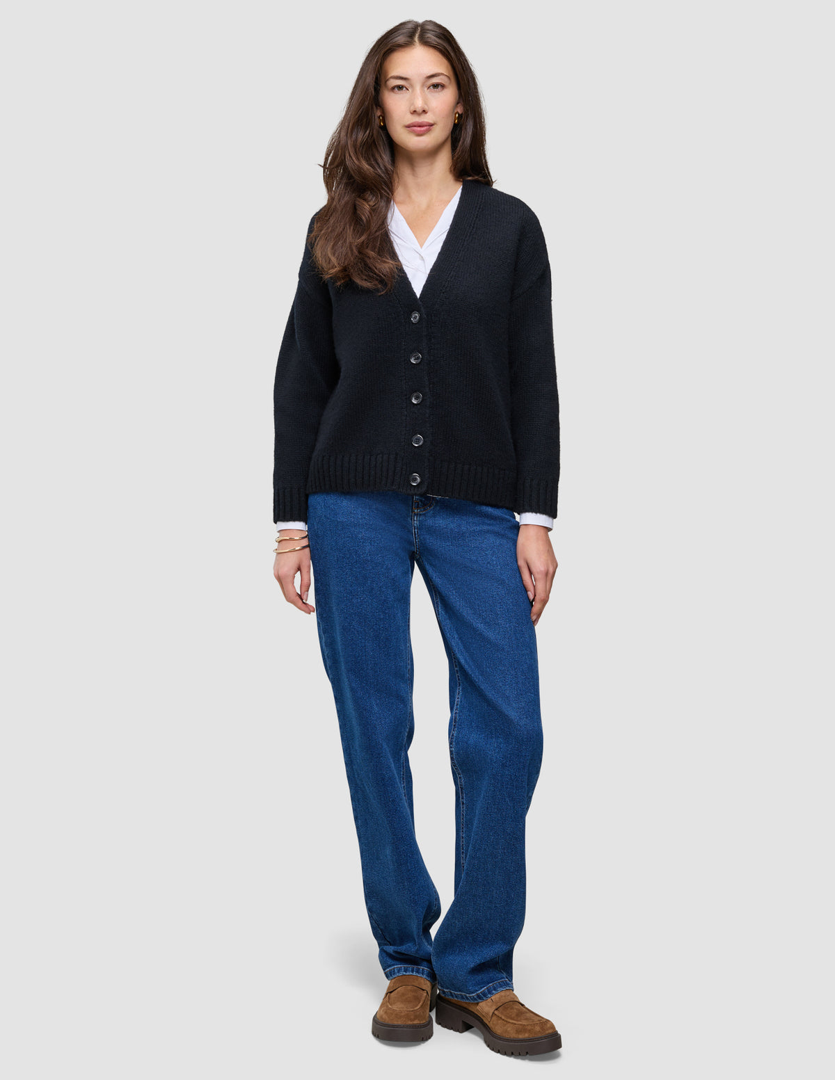 En person som har på seg en svart, grovstrikket, myk ullcardigan for kvinner over en hvit skjorte og blå jeans.