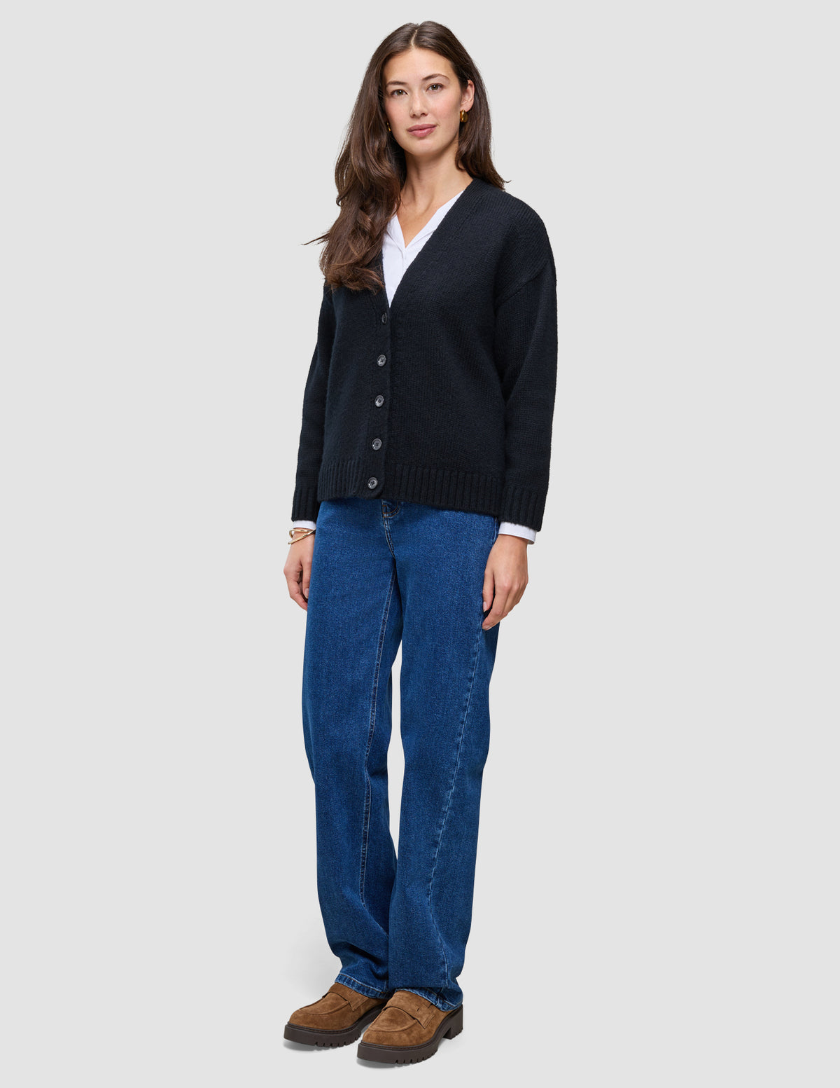 En kvinne som har på seg en svart, grovstrikket, myk ullkofta for kvinner over en hvit skjorte og blå jeans.