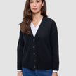 En person som har på seg en svart, tykk og myk strikket cardigan for kvinner over en hvit skjorte og blå jeans.