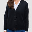Kvinners tykk, myk ullstrikket cardigan i svart, båret over en hvit skjorte og blå jeans.