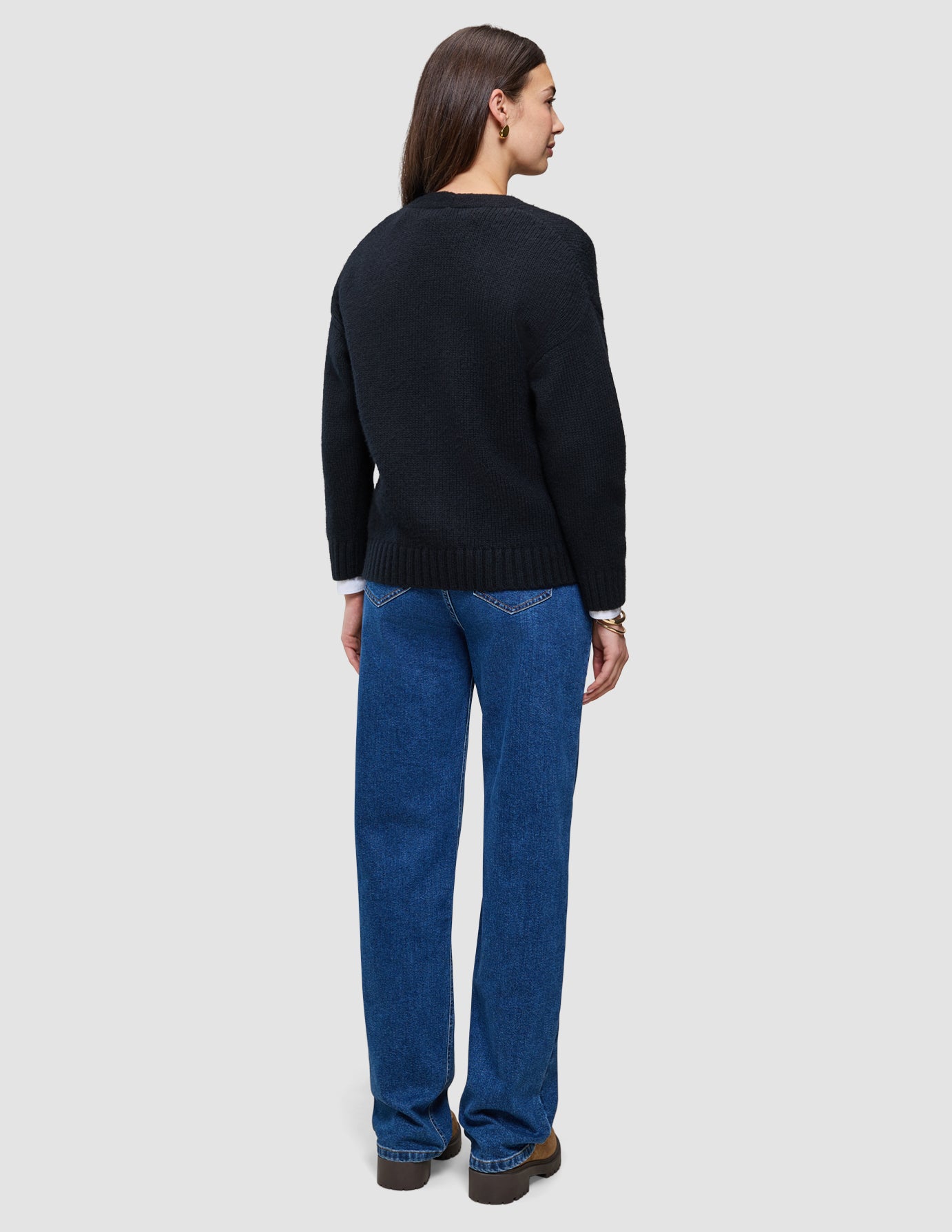 Sett bakfra har personen på seg en svart, tykk og myk ullstrikket cardigan for kvinner over en hvit skjorte og blå jeans.
