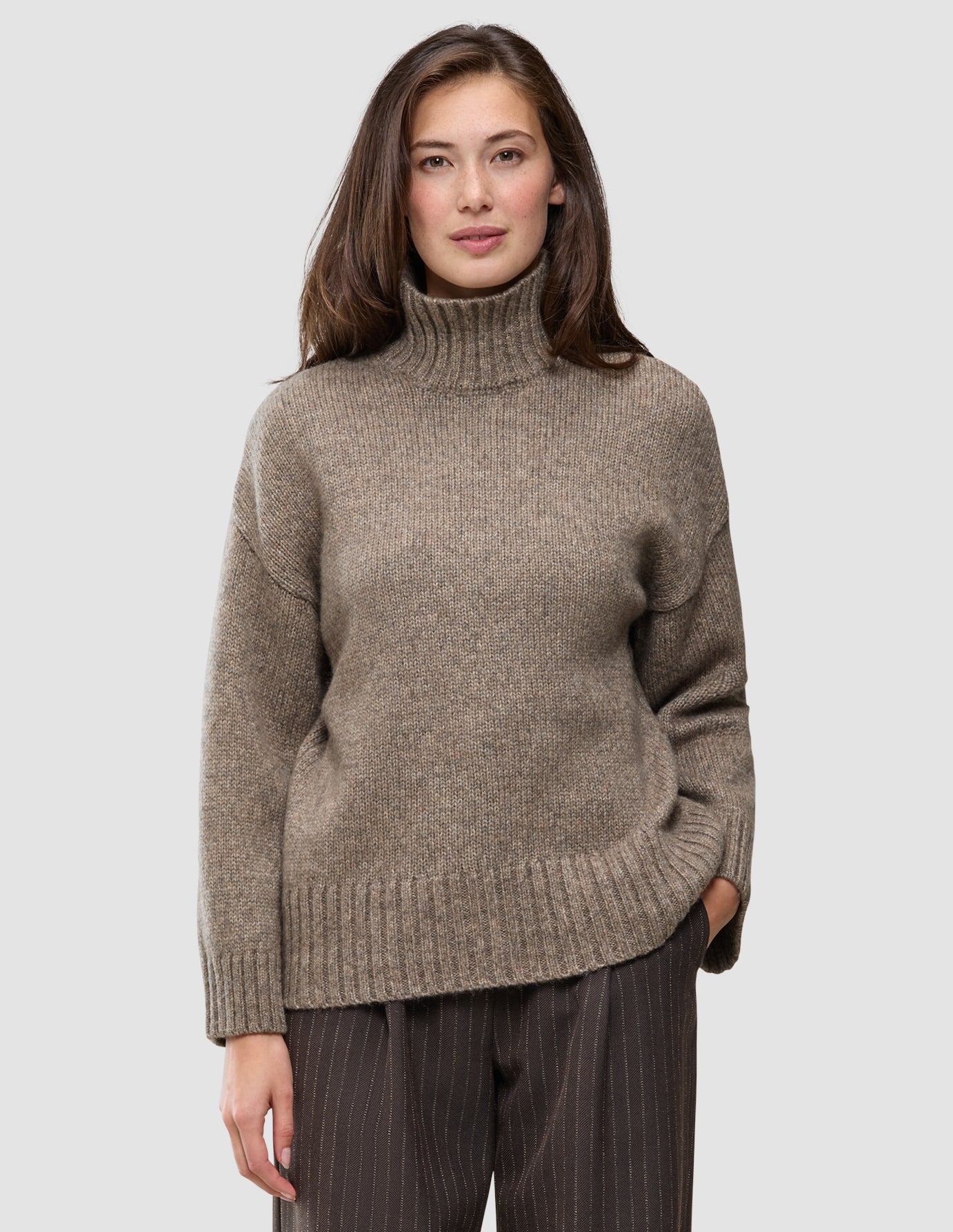 En kvinne iført en taupefarget, grovstrikket turtleneck i myk ull for kvinner, i fargen Taupe Melange.