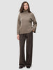En person kledd i en tykk, myk ullstrikket turtleneck for kvinner i fargen taupe melange og brune bukser med smale striper.