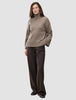 En kvinne kledd i en tykk, myk ullstrikket turtleneck for kvinner i fargen taupe melange og bukser med vid benvidde og smale striper.