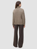 Baksiden av en tykk, myk ullstrikket turtleneck for damer i taupe-melange, kombinert med mørke bukser med smale striper.