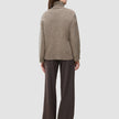 Baksiden av en tykk, myk ullstrikket turtleneck for damer i taupe-melange, kombinert med mørke bukser med smale striper.